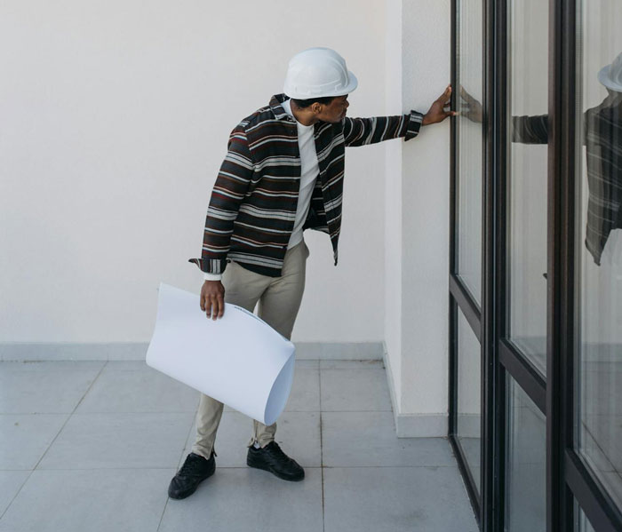 Inspector examining a luxury home's exterior, holding blueprints, wearing a hard hat. Inspector examining a luxury home's exterior, holding blueprints, wearing a hard hat.