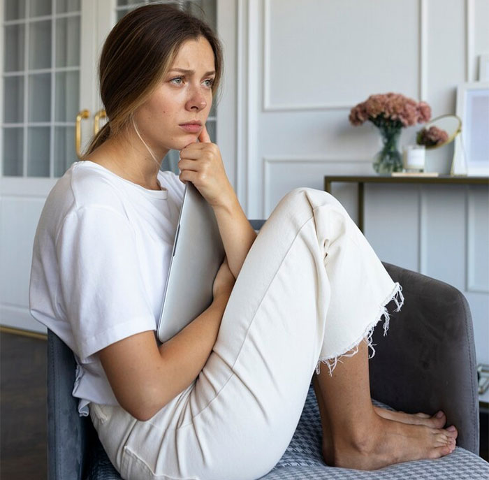 Woman sitting on a sofa, deep in thought about starting a family, holding a laptop in a cozy living room. Woman sitting on a sofa, deep in thought about starting a family, holding a laptop in a cozy living room.
