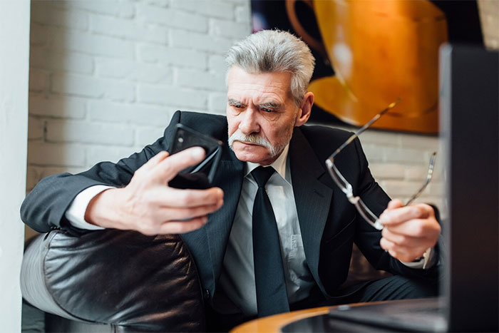 Boss in suit looking at phone angrily, holding glasses, inside modern office setting. Boss in suit looking at phone angrily, holding glasses, inside modern office setting.