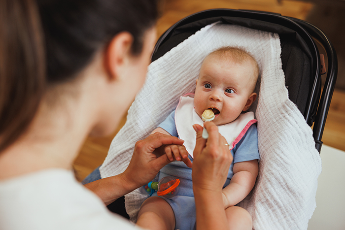 Mom feeds baby in high chair, holding a spoon with food. Mom feeds baby in high chair, holding a spoon with food.