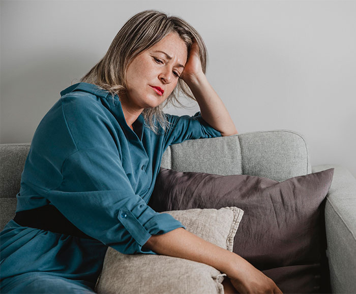 A woman in a blue dress sitting on a sofa, looking contemplative, possibly involved in HOA community drama. A woman in a blue dress sitting on a sofa, looking contemplative, possibly involved in HOA community drama.