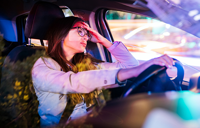 Woman driver looking stressed, resting head on hand, city lights reflecting on car window. Woman driver looking stressed, resting head on hand, city lights reflecting on car window.