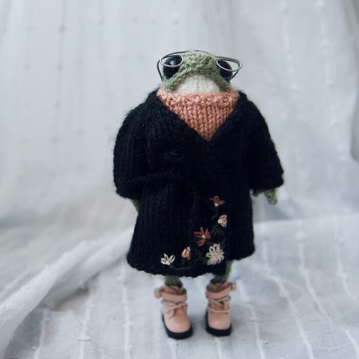 Miniature frog in a knitted outfit and sunglasses, crafted by a French knitter, on a light background.