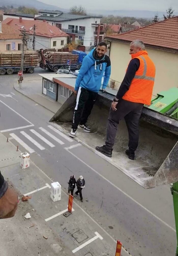 Two employees blatantly ignoring safety protocol while standing unsafely in a raised loader bucket above a street.