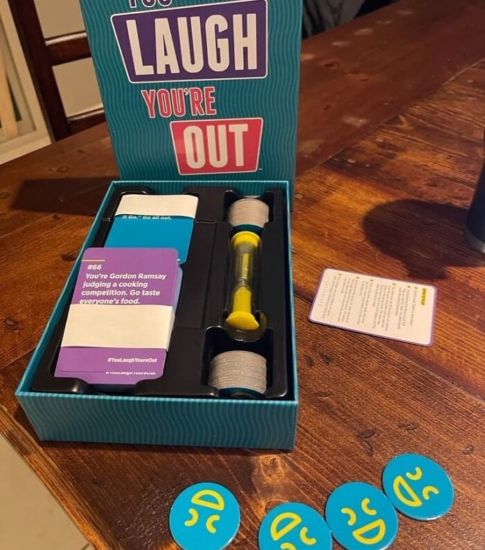 Compact and straightforward game You’re Laugh You’re Out with cards, timer, and tokens on a wooden table.