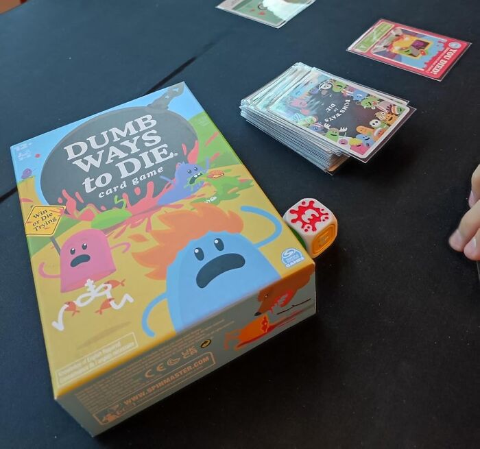 Dumb Ways to Die card game with dice and cards displayed on a black tabletop, example of compact straightforward games.