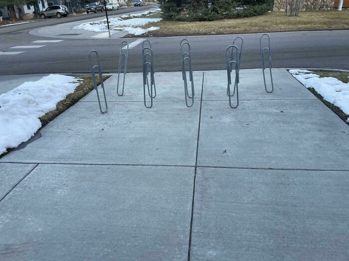 Unique bike rack design creatively shaped like paperclips on a snowy sidewalk corner.