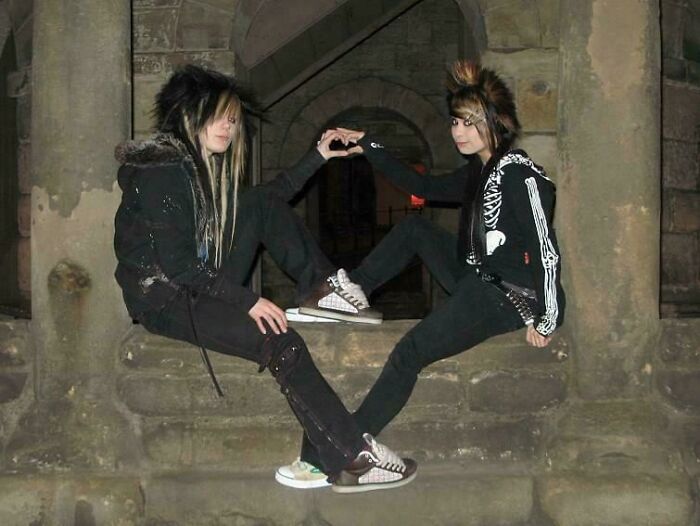 Two people in gothic attire creating a heart shape with their hands, embodying youthful fashion blunder years.