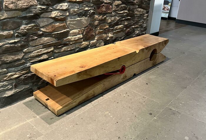 Creative bench design: a large wood piece resembling a clothespin against a stone wall.