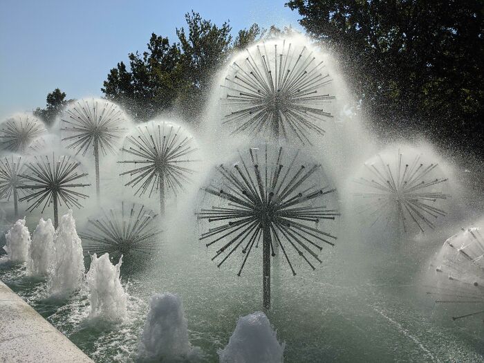 Intricate fountain design resembling dandelions, with water spraying gracefully under sunlight, showcasing designer excellence.