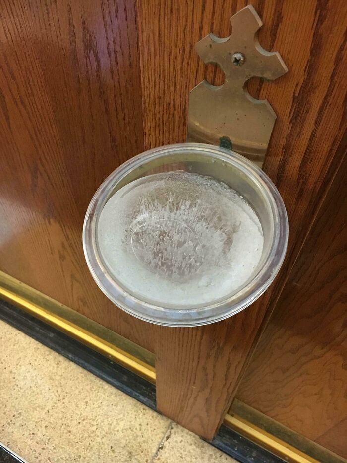 Frozen holy water in a metal basin on a wooden wall, capturing the chill of ice-cold winter.