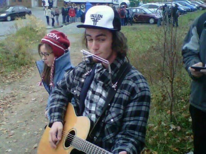 A young person with a harmonica and guitar during an outdoor gathering, showcasing their blunder years.