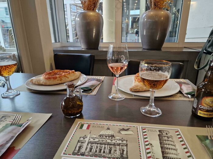 A table setting with drinks, pizza, and infuriating family members' empty chairs in a cozy restaurant.