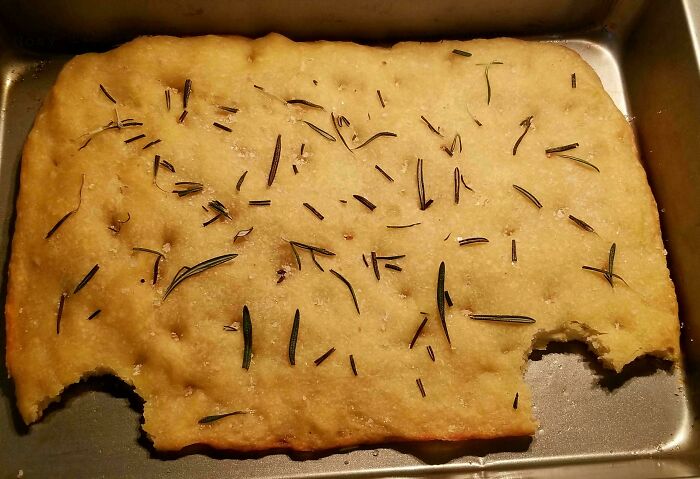 Focaccia bread with a bite missing, baked with rosemary, depicting an annoying family member's action.