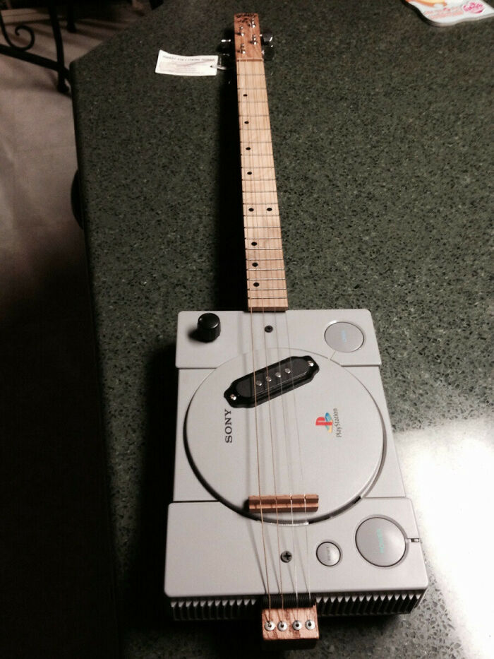 Unique guitar made from a PlayStation console on a green table, showcasing creative craftsmanship.