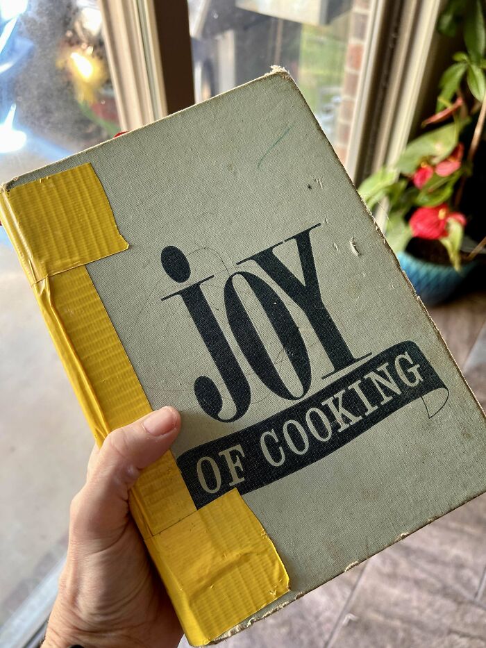 A hand holding a vintage "Joy of Cooking" book with yellow tape, great gift idea for amazing mothers-in-law.