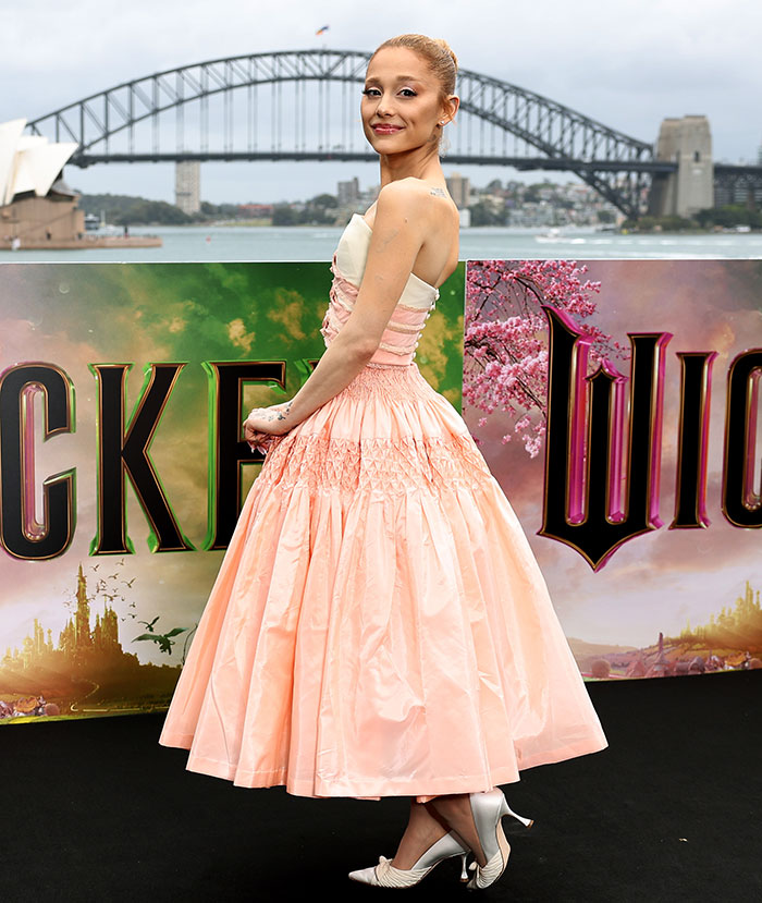 Robotic Thing: Woman in elegant peach dress at movie premiere, standing in front of scenic backdrop and bridge. Robotic Thing: Woman in elegant peach dress at movie premiere, standing in front of scenic backdrop and bridge.