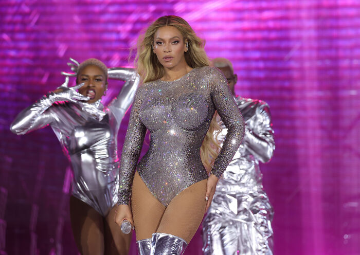 Popstar Beyoncé performs in a dazzling silver outfit with vibrant pink background and backup dancers. Popstar Beyoncé performs in a dazzling silver outfit with vibrant pink background and backup dancers.