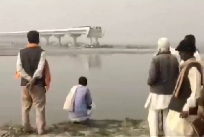People observing an unfinished bridge across a river, raising safety concerns about fatal car crashes. People observing an unfinished bridge across a river, raising safety concerns about fatal car crashes.