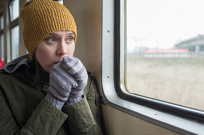 Passenger looking anxious on train's scenic route, wearing a knit hat and gloves, gazing out the window. Passenger looking anxious on train's scenic route, wearing a knit hat and gloves, gazing out the window.