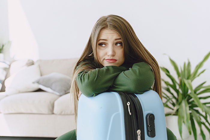 Passenger looking distressed, leaning on a blue suitcase indoors after a train detour. Passenger looking distressed, leaning on a blue suitcase indoors after a train detour.