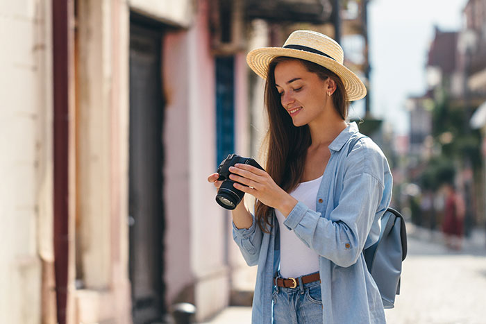 Woman with a camera smiling on a sunny street, wearing a straw hat and denim shirt. Woman with a camera smiling on a sunny street, wearing a straw hat and denim shirt.
