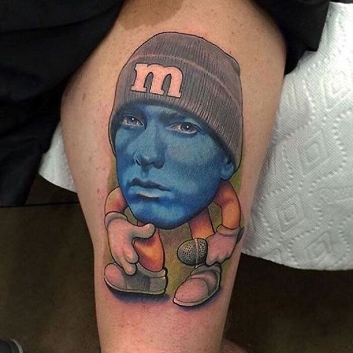 Epic tattoo fail featuring a blue cartoon character with a human face and a beanie on a person's leg. Epic tattoo fail featuring a blue cartoon character with a human face and a beanie on a person's leg.