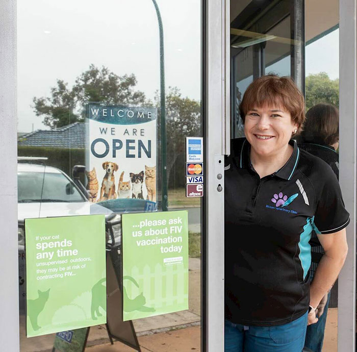 A woman stands at the entrance of a veterinary clinic promoting animal welfare, with signs about FIV vaccination. A woman stands at the entrance of a veterinary clinic promoting animal welfare, with signs about FIV vaccination.