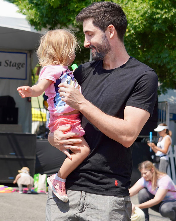 Bobbi Althoff’s husband, smiling and holding a young child at an outdoor event, with people and trees visible in the background. Bobbi Althoff’s husband, smiling and holding a young child at an outdoor event, with people and trees visible in the background.