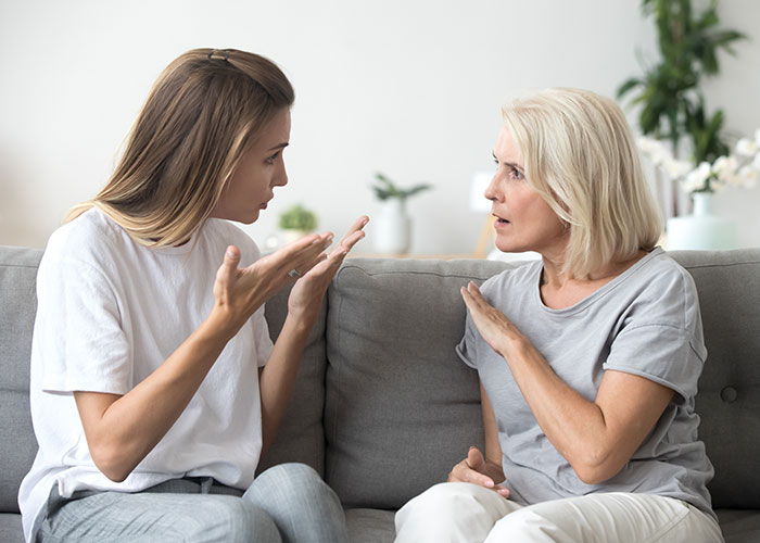 Two women sitting on a sofa, engaged in a heated discussion about family holidays. Two women sitting on a sofa, engaged in a heated discussion about family holidays.