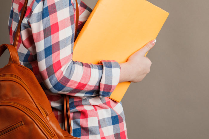 Teen holding yellow folder, wearing a plaid shirt and backpack, symbolizes an academic setting involving a picked-on student. Teen holding yellow folder, wearing a plaid shirt and backpack, symbolizes an academic setting involving a picked-on student.