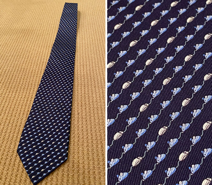 Designer tie with intricate navy pattern, close-up and full view on beige background.