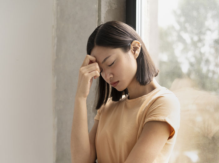 Woman looking stressed, leaning against a window, feeling uneasy about Japanese culture-themed decor. Woman looking stressed, leaning against a window, feeling uneasy about Japanese culture-themed decor.