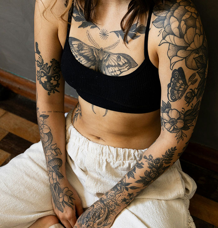 Young person with modern tattoos, showcasing floral and animal designs on arms and chest, illustrating 2024 tattoo trends. Young person with modern tattoos, showcasing floral and animal designs on arms and chest, illustrating 2024 tattoo trends.