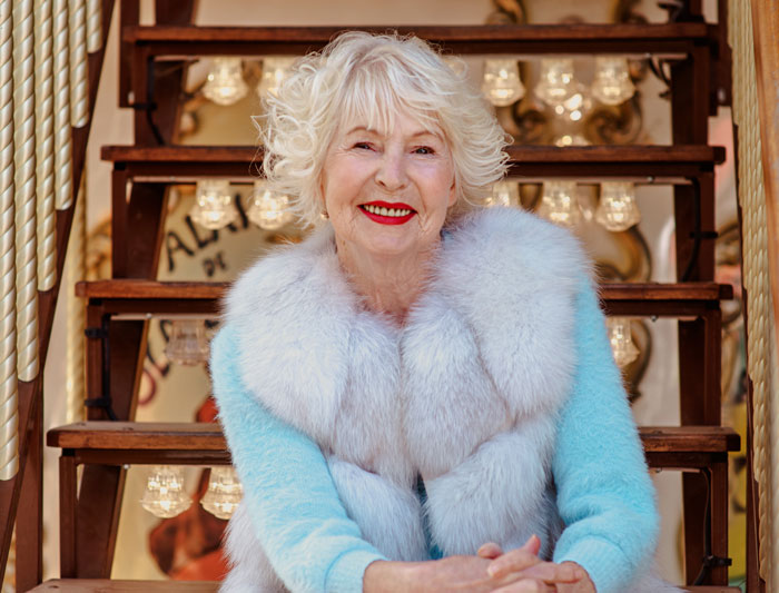 Elderly woman in a blue coat sitting on stairs, smiling confidently. Elderly woman in a blue coat sitting on stairs, smiling confidently.