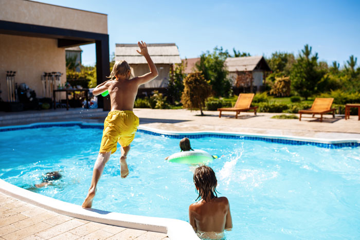 Kids playing alone in a pool, with one jumping in and others swimming under a clear blue sky. Kids playing alone in a pool, with one jumping in and others swimming under a clear blue sky.