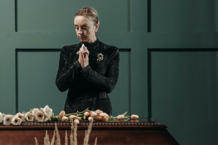 Grieving mother-in-law standing by a casket with flowers, looking emotional and contemplative. Grieving mother-in-law standing by a casket with flowers, looking emotional and contemplative.