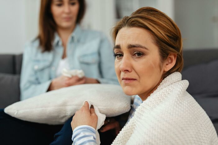 Grieving mother-in-law looking upset on a couch, while another woman listens in the background. Grieving mother-in-law looking upset on a couch, while another woman listens in the background.