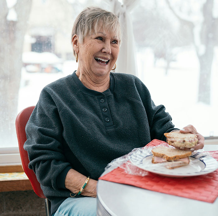 Smiling elderly woman enjoying a meal, showcasing a family setting. Smiling elderly woman enjoying a meal, showcasing a family setting.