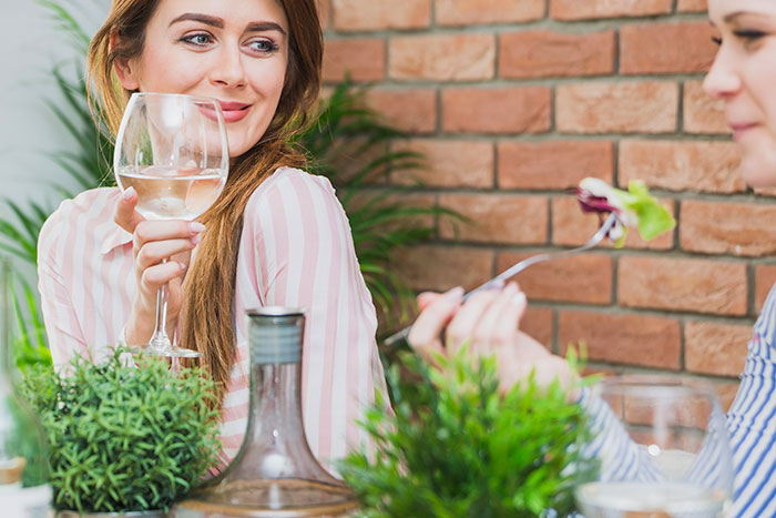 Woman in a pink shirt holding a wine glass, engaging in conversation over a meal, conveying honesty and communication. Woman in a pink shirt holding a wine glass, engaging in conversation over a meal, conveying honesty and communication.