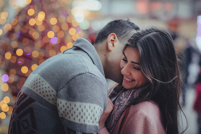 Couple embracing in front of festive lights, capturing a moment of romance during a holiday season. Couple embracing in front of festive lights, capturing a moment of romance during a holiday season.