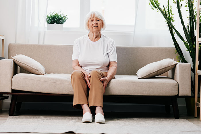 Elderly woman sitting on a beige sofa in a bright living room, looking pensive. Elderly woman sitting on a beige sofa in a bright living room, looking pensive.