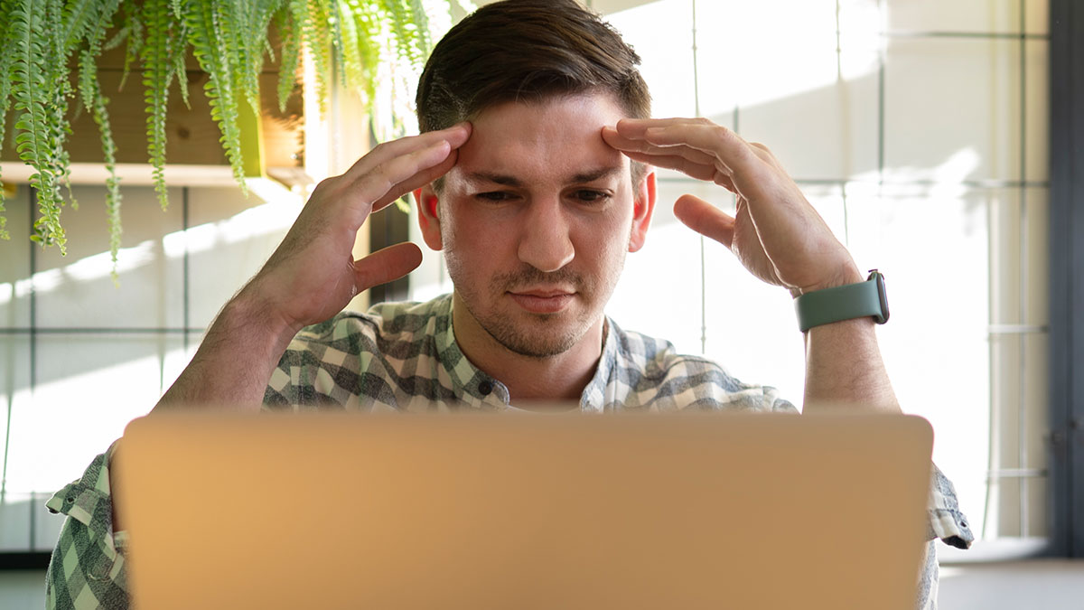 Man looking stressed while using laptop, reacting to wild posts from app dedicated to neighbors.