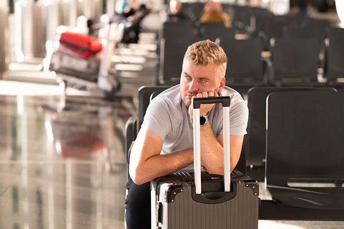 Man at airport lounges on suitcase, appearing frustrated, amid empty seats. Man at airport lounges on suitcase, appearing frustrated, amid empty seats.