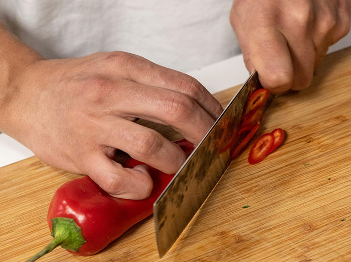 Person slicing red pepper on wooden board, setting a trap for food-thieving roommate. Person slicing red pepper on wooden board, setting a trap for food-thieving roommate.