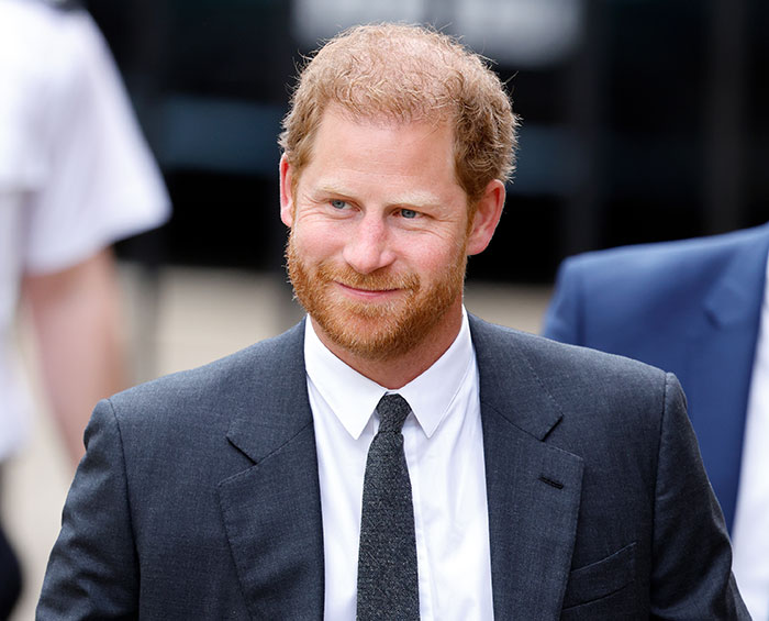 Prince Harry in a gray suit smiling while walking outside, related to neck tattoo video. Prince Harry in a gray suit smiling while walking outside, related to neck tattoo video.