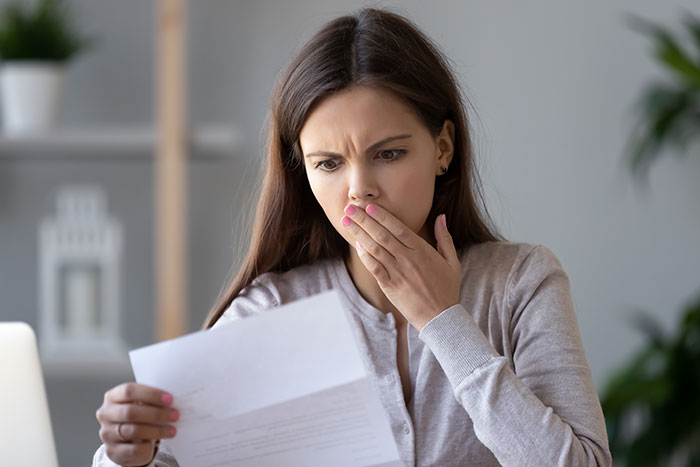 Woman looking shocked at a document, possibly related to unexpected wedding costs. Woman looking shocked at a document, possibly related to unexpected wedding costs.