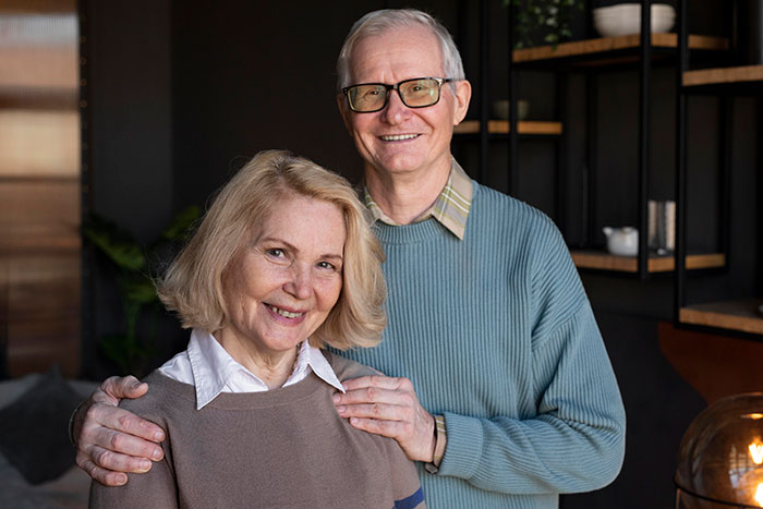 Elderly couple smiling indoors, with warm lighting and modern decor in the background. Elderly couple smiling indoors, with warm lighting and modern decor in the background.