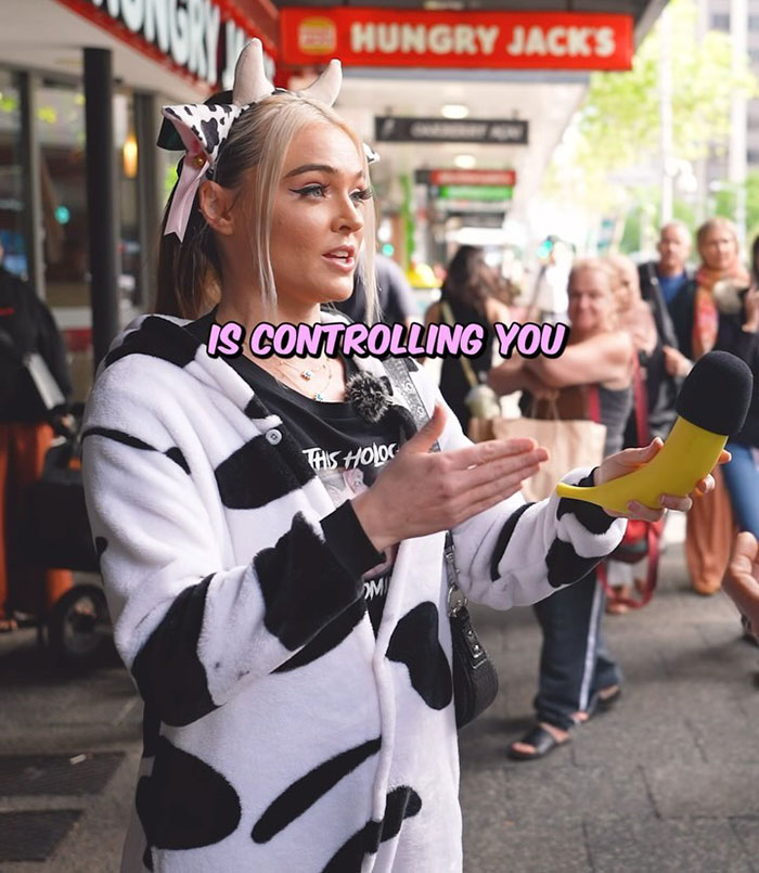 Vegan activist in cow-patterned outfit holding a microphone, advocating against animal slavery on a busy street. Vegan activist in cow-patterned outfit holding a microphone, advocating against animal slavery on a busy street.