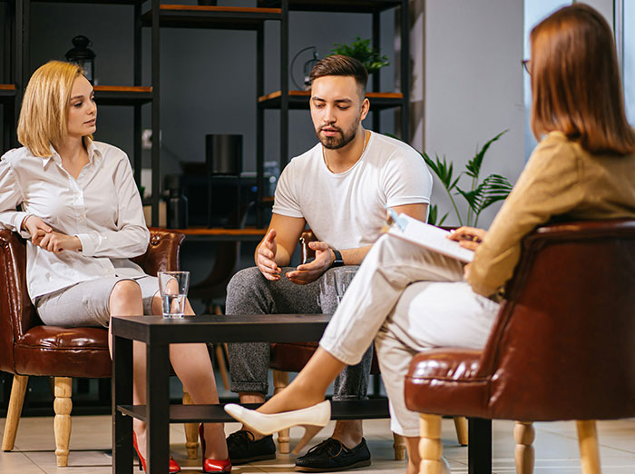 Group discussion in a meeting room with a woman and two others, sharing a story of being cheated on. Group discussion in a meeting room with a woman and two others, sharing a story of being cheated on.